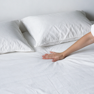 Mano che stende il coprimaterasso antiacaro Acarbasic® con due copricuscini antiacaro bianchi sul letto