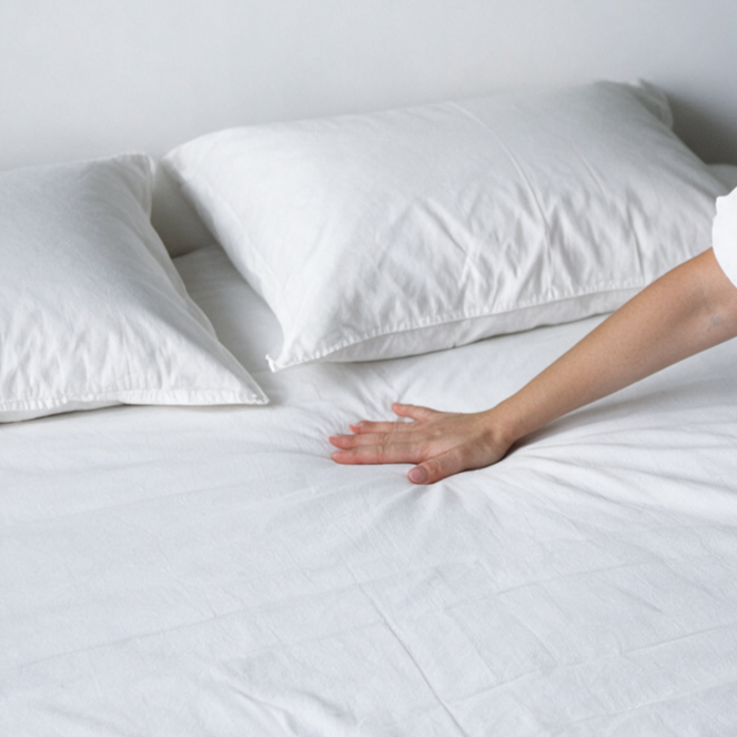 Mano che stende il coprimaterasso antiacaro Acarbasic® con due copricuscini antiacaro bianchi sul letto