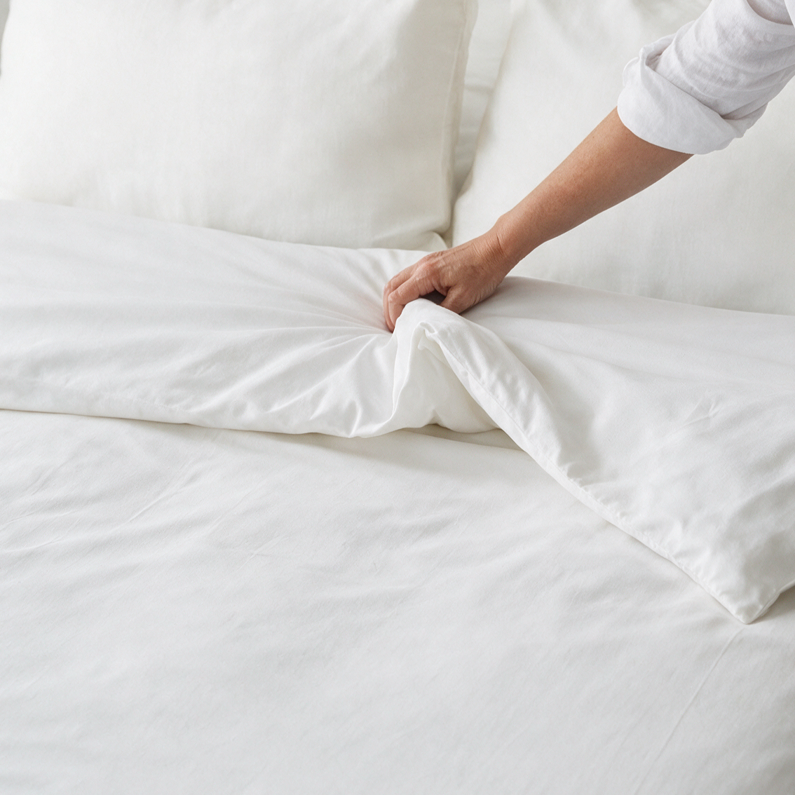Mano che sistema il copripiumino antiacaro Acarbuster® sul letto con coprimaterasso e copricuscini antiacaro