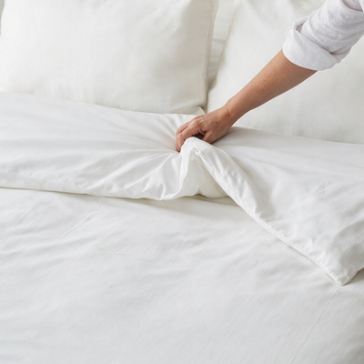 Mano che sistema il copripiumino antiacaro Acarbuster® sul letto con coprimaterasso e copricuscini antiacaro