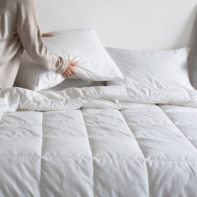 Persona che sistema il copricuscino antiacaro Acarbuster® su un letto con piumino antiacaro trapuntato