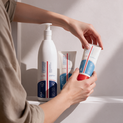 Mano che prende una crema magra per pelle secca atopica da un set con detergente Envisoap®